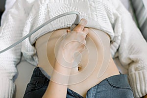 Cropped image of hand of female doctor moving ultrasound scanner on young woman`s stomach in modern medical center