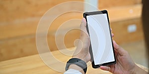 Cropped image hands are holding a white blank screen smartphone in the comfortable living room