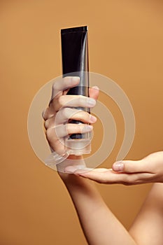 Cropped image of hands holds big tube with cosmetic care eco product against beige background. Copy space for your ad