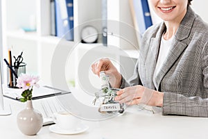 Cropped image of happy businesswoman putting money in glass jar for travel