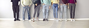 Cropped image of the legs of people in ordinary clothes and shoes standing in a row near the wall.