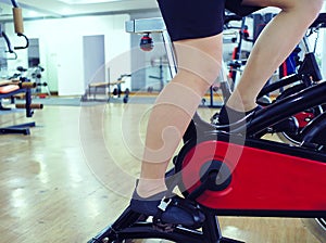 Cropped image of legs of young healthy man exercising on bike machine at sport gym. Fitness and workout concept