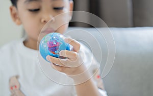 Cropped image of a lilltle Asain boy holds the globe on his hand and looks at it in the living room at home