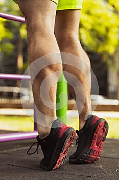 Cropped image of male muscular legs, feet in sportshoes standing on tiptoes during sports training outdoors