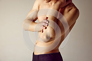 Cropped image of male shirtless body against grey studio background. Man holding elbow, suffering from pain