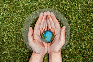 cropped image of man holding earth model in hands above green grass, earth