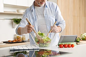 Cropped image of mature man cooking salad using tablet