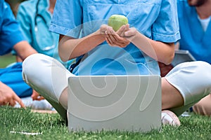 cropped image of medical student holding ripe green apple in hands and sitting