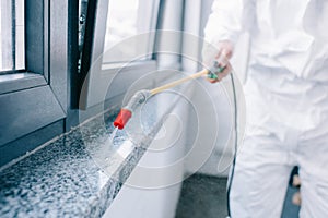 cropped image of pest control worker spraying pesticides on windowsill