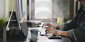 Cropped image of photographer hands typing on wireless keyboard and using mouse while sitting in front computer monitor.