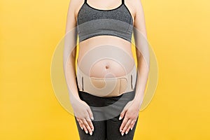 Cropped image of pregnancy belt dressed on pregnant woman for reducing pain in the back at yellow background with copy space.