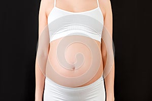 Cropped image of pregnant woman`s belly at black background. Future mom in white underwear. Parenthood concept. Copy space