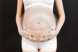 Cropped image of pregnant woman in underwear wearing maternity belt to reduce pain in the back at black background with copy space