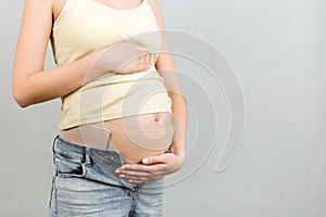 Cropped image of pregnant woman wearing elastic bandage against pain in the back at gray background with copy space. Orthopedic