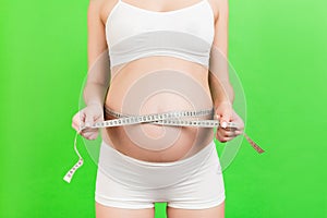 Cropped image of pregnant woman in white underwear measuring her abdomen to check baby development. Centimeter tape measure at