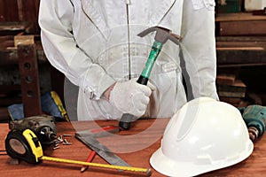 Cropped image of professional young worker with safety uniform holding hammer with other tools on wood workbench in carpentry work