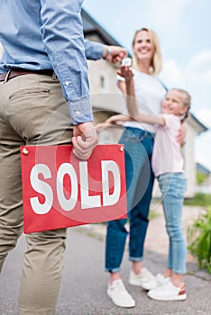 cropped image of realtor with sold sign giving key to young woman