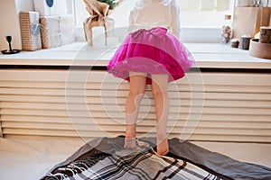 Cropped image and rear view of cute little child girl standing on the bed by window and wainting Christmas eve. Christmas