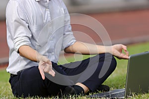 Cropped image of relaxed young Asian business man with laptop doing yoga position on the green grass.