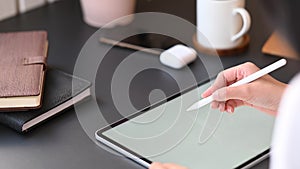 Cropped image of secretary woman`s hand holding stylus pen wile writing on computer tablet.