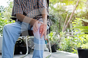 Cropped image of senior man sitting on chair in the garden and having knee pain