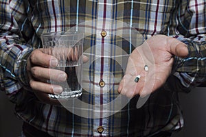 Cropped image of a sick person holding a tablet and a glass of water, on a gray background, hands of a working man