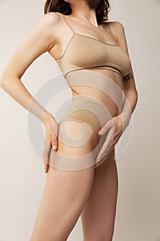 Cropped image of slim female body in beige underwear isolated over grey studio background. Smooth skin