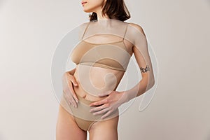 Cropped image of slim female body in beige underwear isolated over grey studio background. Taking care after skin