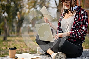 Cropped image of smart Asian female college student using laptop on a bench in campus park