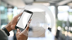 Cropped image of smart man`s hands holding and using a cropped black smartphone with white blank screen.