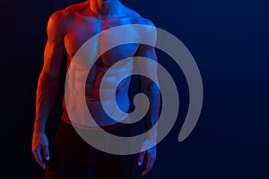Cropped image of a strong athletic young man model showing six pack abs, over dark neon background. Horizontal shot