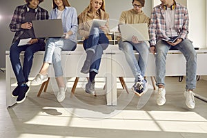 Cropped image of students sitting on the desks with modern gadgets and preparing for lectures.