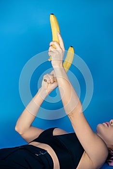 cropped image of stylish girl lying and holding bananas in hands in front of her photo