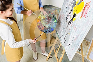 cropped image of teacher and pupil choosing paint on palette in workshop of