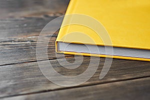 A cropped image of thick book with yellow textured hardcover on a wooden desktop with copy space for text. Template for
