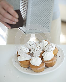 Cropped image of woman grating chocolate on cupcakes at counter photo