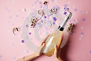 cropped image of woman holding bottle of champagne above confetti on party table