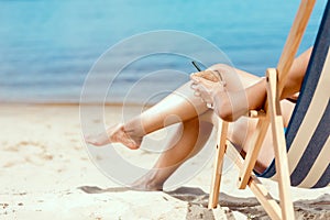 cropped image of woman holding cocktail in coconut shell and laying on deck chair