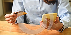 Cropped image of a woman is holding a credit card and smartphone in hands.