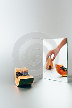 cropped image of woman holding yellow papaya reflecting in mirror