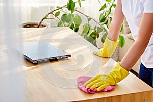 Cropped image of woman in white shirt and yellow protective rubber gloves cleaning at home and wiping dust on wooden tablel. photo