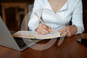 Cropped image of a woman writing some ideas down in her book, working remotely at a coffee shop