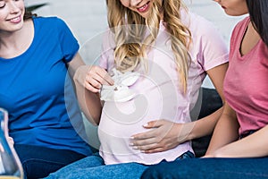 cropped image of women choosing baby shoes with pregnant friend
