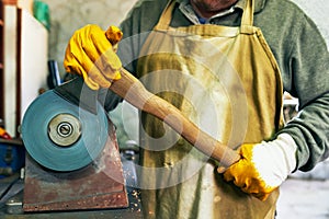 Cropped image of worker adult man manufacturing in his workshop. Senior man grinding the hatcher with sparks in repair shop
