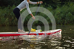 Cropped image of young Caucasian woman, sportsman, tourist standing on paddle board, SUP, practicing alone. Active life