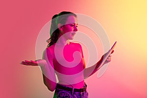 Cropped image of young girl reading news from tablet isolated over gradient studio background in neon lights