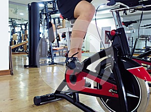 Cropped image of young healthy man exercising on bike machine at sport gym. Fitness and workout concept