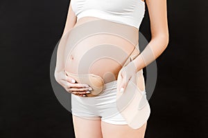 Cropped image of young pregnant woman in underwear dressing pregnancy bandage on her belly to make the backache go away at black