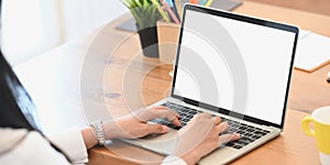 Cropped image of young western woman hands typing on white blank screen computer laptop that putting on wooden desk.