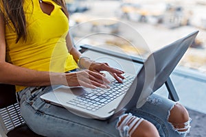 Cropped image of young woman holding a laptop on lap typing keyboard indoors in public place